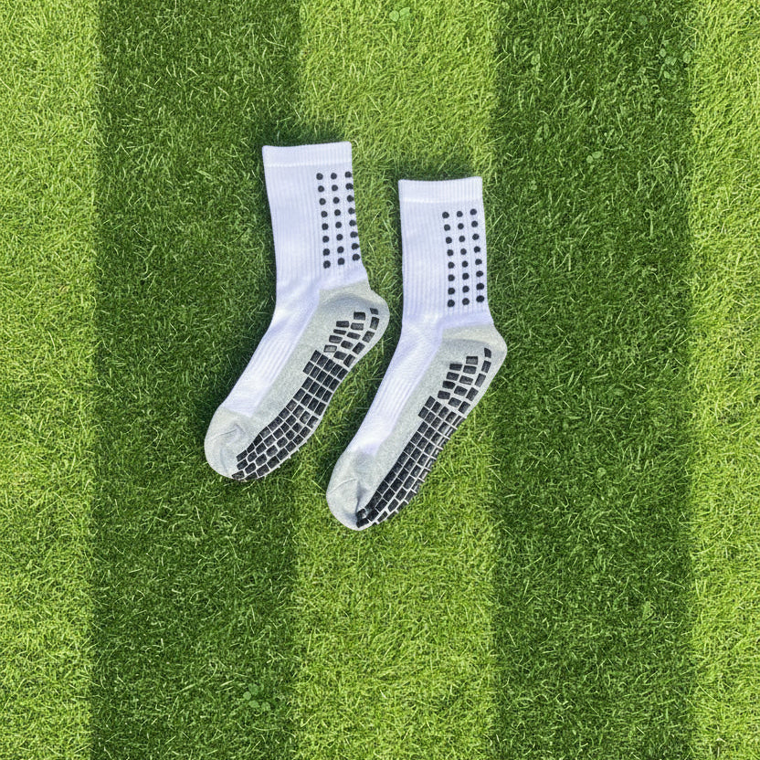A pair of white athletic cleats lying on green grass outdoors.